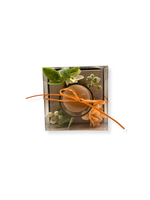lumanare decorativa in pahar cu decor floral peach, frunze pastel si bobite albe, ambalata in cutie transparenta cu funda portocalie